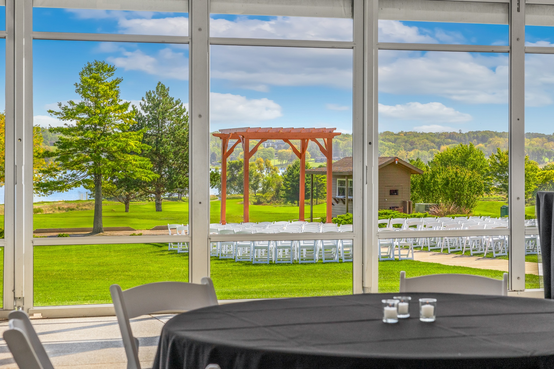 View from the pavilion of an outdoor ceremony setup with pergola and lake beyond